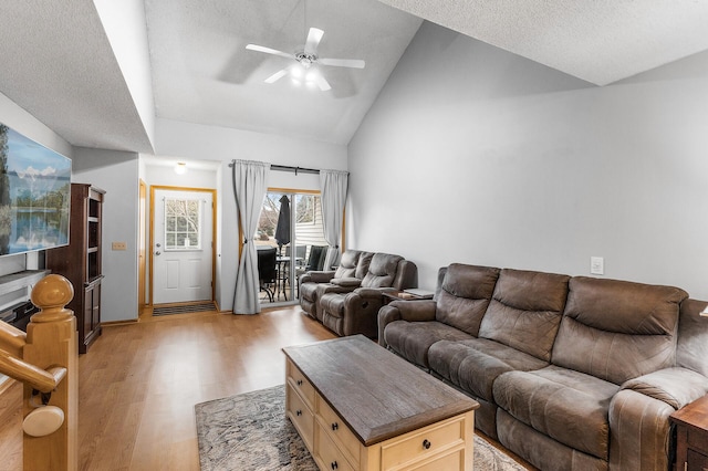 living room with ceiling fan, light wood-type flooring, a textured ceiling, and high vaulted ceiling