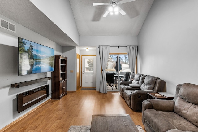 living room with ceiling fan, light wood-type flooring, and vaulted ceiling