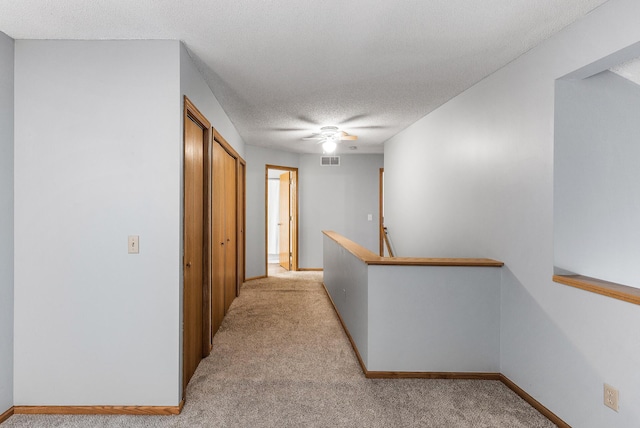 hall featuring light carpet and a textured ceiling