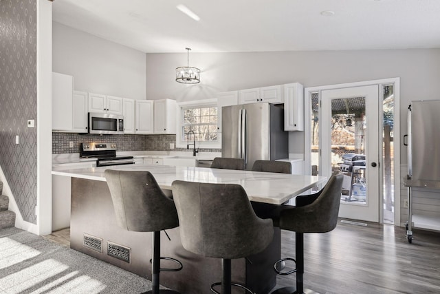 kitchen featuring decorative light fixtures, white cabinets, a kitchen island, and appliances with stainless steel finishes