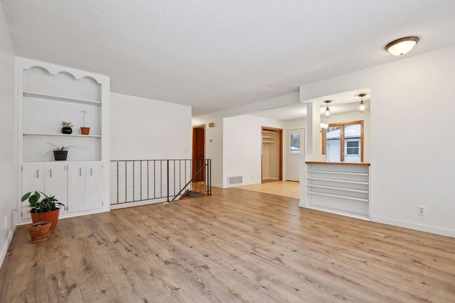 unfurnished living room with a textured ceiling, light wood-type flooring, and built in shelves