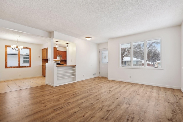 unfurnished living room with a textured ceiling, an inviting chandelier, and light hardwood / wood-style floors