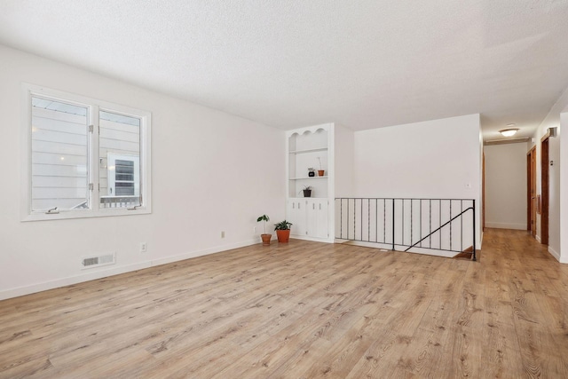 spare room with a textured ceiling and light hardwood / wood-style flooring