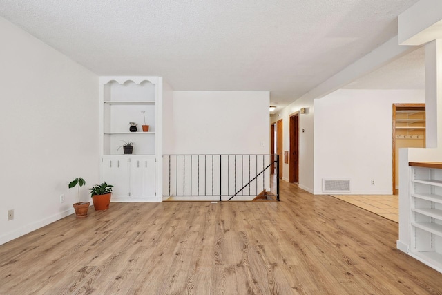 empty room with a textured ceiling, built in shelves, and light hardwood / wood-style flooring