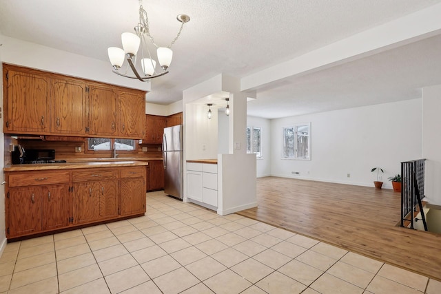 kitchen featuring a textured ceiling, pendant lighting, a chandelier, stainless steel fridge, and light tile patterned flooring