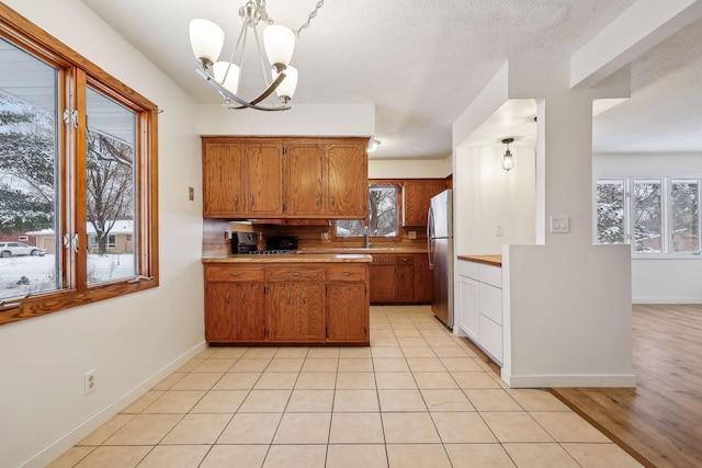 kitchen featuring a chandelier, stainless steel refrigerator, light tile patterned floors, sink, and decorative light fixtures