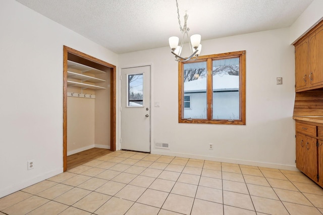 unfurnished dining area featuring a textured ceiling, an inviting chandelier, plenty of natural light, and light tile patterned floors