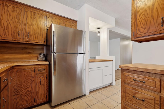 kitchen with white cabinetry, a textured ceiling, light tile patterned flooring, wood counters, and stainless steel refrigerator