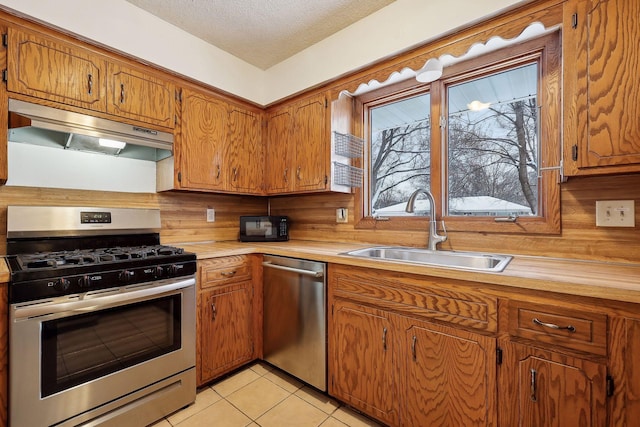 kitchen with sink, a textured ceiling, light tile patterned floors, backsplash, and appliances with stainless steel finishes