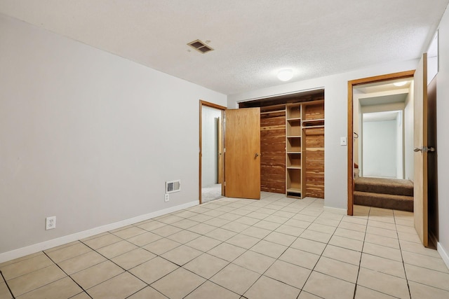 unfurnished bedroom featuring a textured ceiling, a walk in closet, a closet, and light tile patterned floors