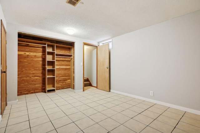 unfurnished bedroom with light tile patterned floors, a closet, wood walls, and a textured ceiling