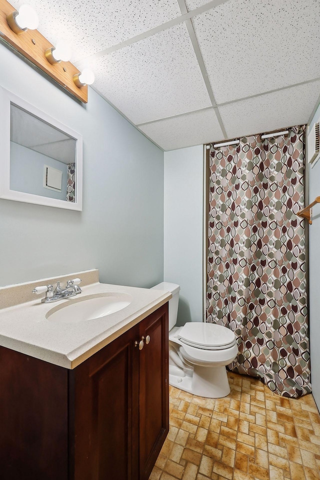 bathroom featuring toilet, vanity, and a drop ceiling