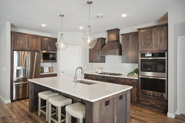 kitchen with dark hardwood / wood-style flooring, custom range hood, stainless steel appliances, sink, and a center island with sink