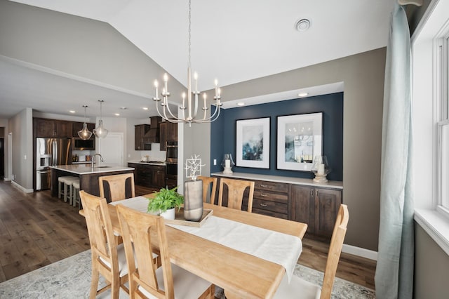 dining area featuring sink, dark wood-type flooring, vaulted ceiling, and an inviting chandelier