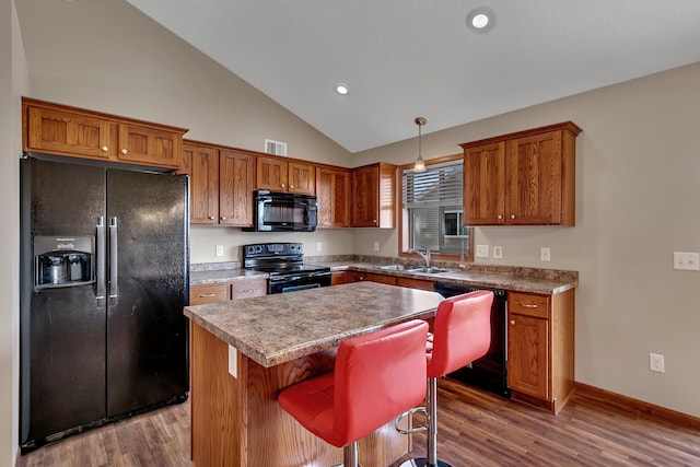 kitchen with brown cabinets, black appliances, a sink, wood finished floors, and a center island