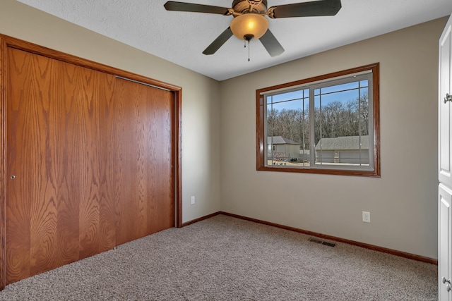 unfurnished bedroom with visible vents, a textured ceiling, a closet, carpet floors, and baseboards