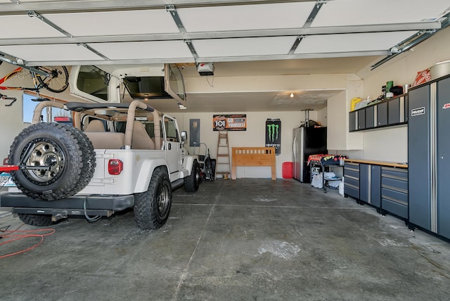 garage featuring electric panel, a garage door opener, and freestanding refrigerator