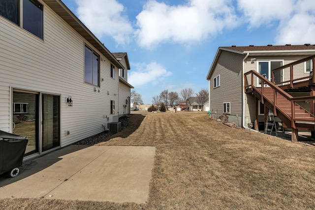 view of side of home with a patio, central air condition unit, stairway, and a lawn