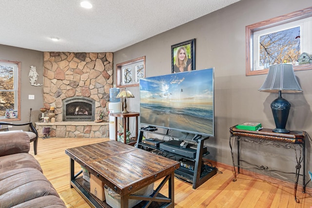 living room featuring a textured ceiling, hardwood / wood-style flooring, and a stone fireplace