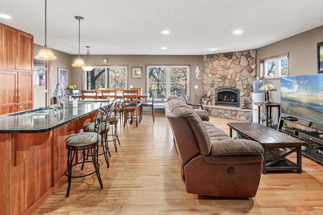 living room featuring a textured ceiling, a stone fireplace, a healthy amount of sunlight, and sink