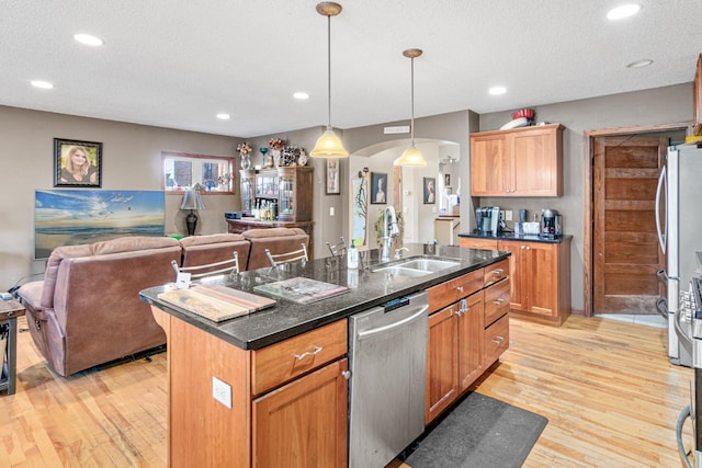 kitchen featuring appliances with stainless steel finishes, sink, a center island with sink, decorative light fixtures, and light hardwood / wood-style floors