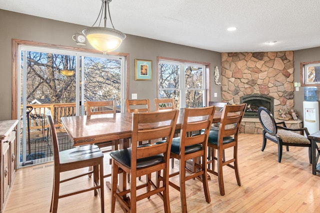 dining area with light hardwood / wood-style floors, a stone fireplace, and a textured ceiling