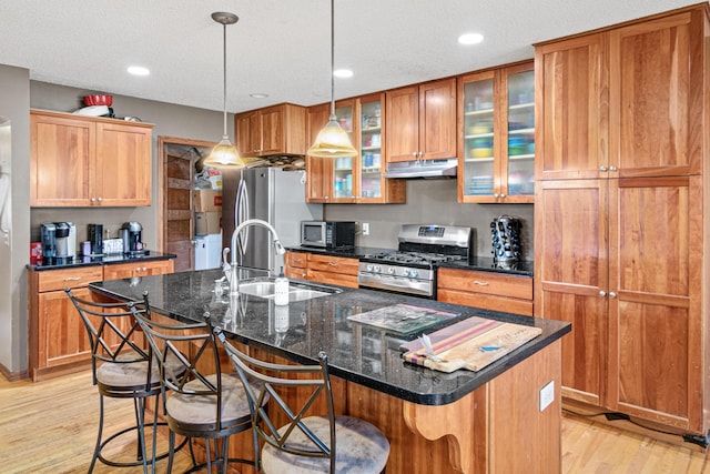 kitchen featuring a breakfast bar, sink, dark stone countertops, an island with sink, and gas stove