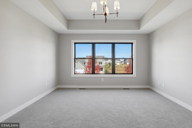 carpeted empty room featuring a raised ceiling and an inviting chandelier