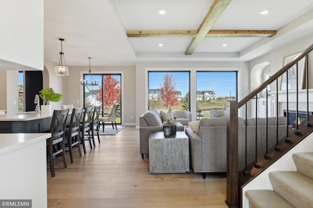 living room featuring a notable chandelier, light hardwood / wood-style floors, a healthy amount of sunlight, and beam ceiling