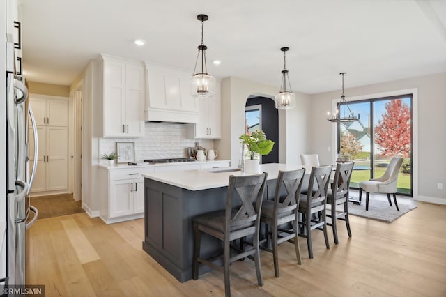 kitchen featuring decorative light fixtures, white cabinetry, a kitchen island with sink, and light hardwood / wood-style flooring