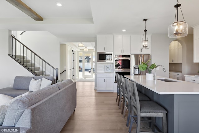 kitchen featuring a center island with sink, sink, hanging light fixtures, light hardwood / wood-style flooring, and stainless steel appliances