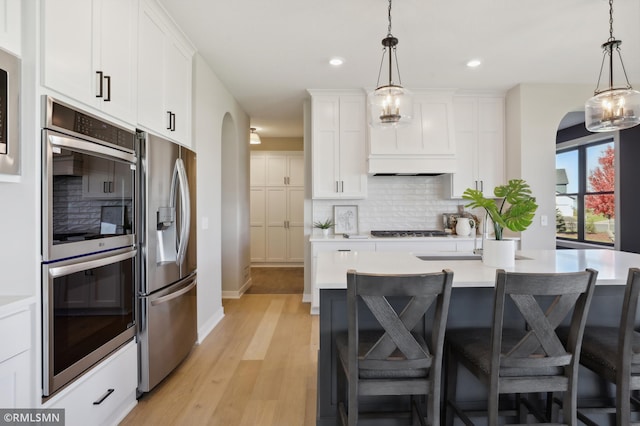 kitchen with appliances with stainless steel finishes, light hardwood / wood-style floors, white cabinetry, and pendant lighting