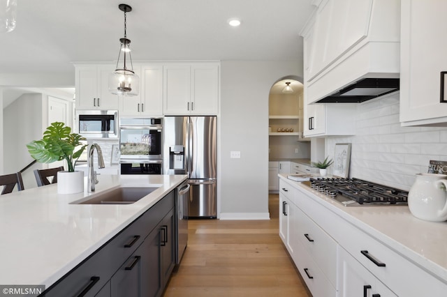 kitchen featuring appliances with stainless steel finishes, custom range hood, sink, white cabinetry, and hanging light fixtures