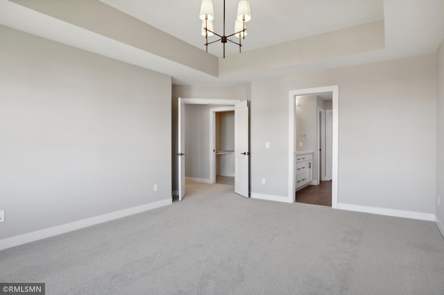 unfurnished bedroom featuring ensuite bathroom, dark carpet, and a notable chandelier