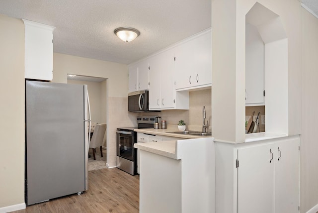 kitchen with sink, appliances with stainless steel finishes, a textured ceiling, white cabinets, and light wood-type flooring