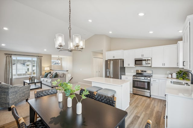 dining area with light hardwood / wood-style floors, vaulted ceiling, a notable chandelier, and sink