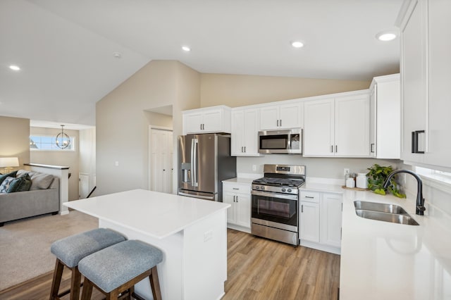 kitchen with appliances with stainless steel finishes, light wood-type flooring, sink, white cabinetry, and lofted ceiling