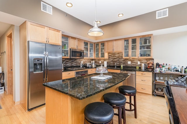 kitchen with a kitchen island, light wood-type flooring, decorative light fixtures, and appliances with stainless steel finishes