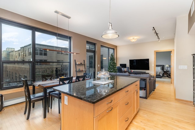 kitchen with decorative light fixtures, light hardwood / wood-style floors, a kitchen island, and dark stone counters