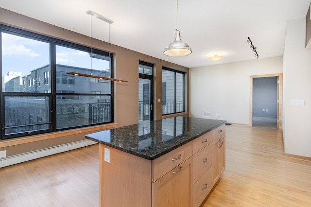 kitchen featuring dark stone countertops, hanging light fixtures, a center island, baseboard heating, and light hardwood / wood-style flooring