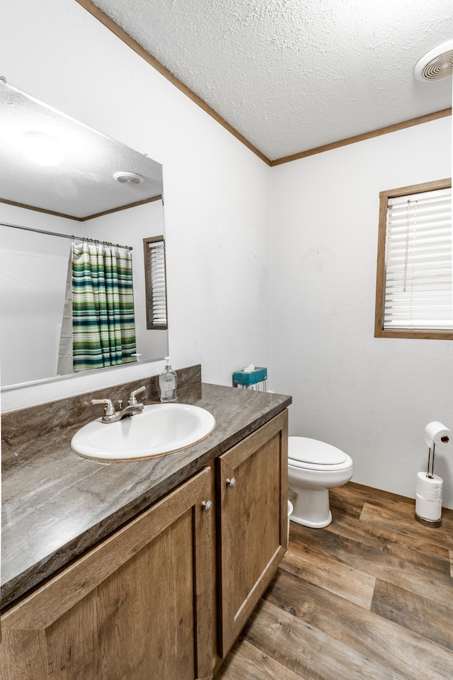 bathroom with ornamental molding, vanity, a textured ceiling, wood-type flooring, and toilet