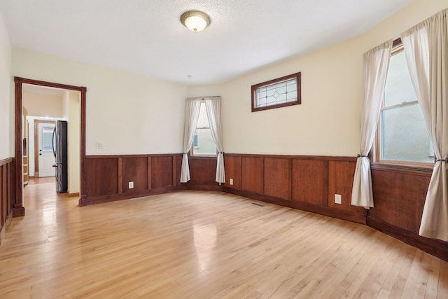 spare room with wood walls, a textured ceiling, and light hardwood / wood-style flooring