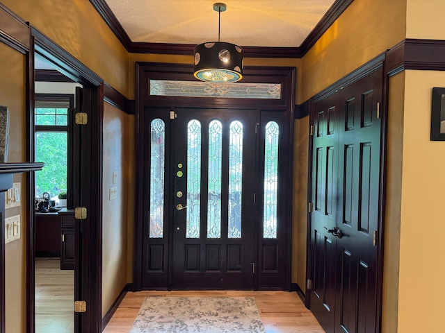 entryway with light hardwood / wood-style floors, ornamental molding, and a textured ceiling