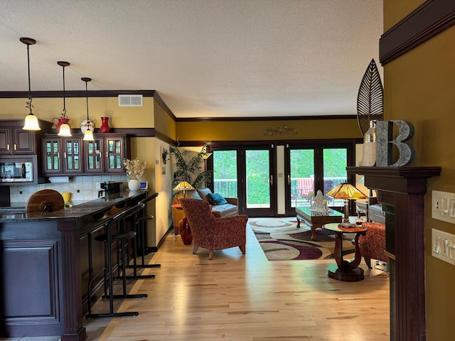 living room featuring a textured ceiling, light hardwood / wood-style floors, crown molding, and bar