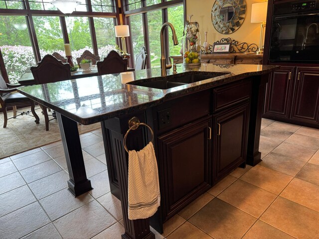 kitchen featuring dark stone counters, a kitchen breakfast bar, sink, black oven, and light tile patterned flooring