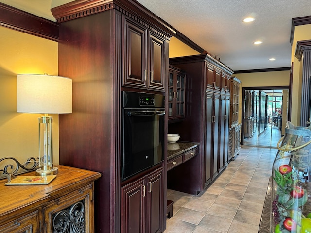 kitchen featuring ornamental molding, a textured ceiling, dark brown cabinetry, dark stone countertops, and black oven