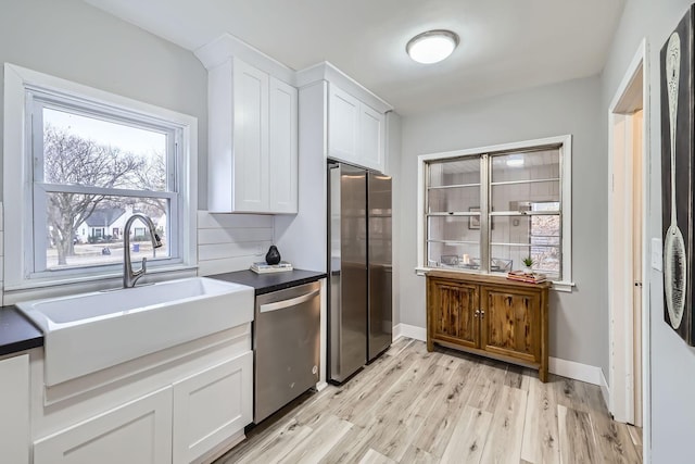 kitchen with white cabinets, sink, light wood-type flooring, appliances with stainless steel finishes, and tasteful backsplash