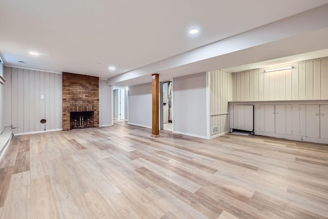 basement with wood walls, light wood-type flooring, and a brick fireplace