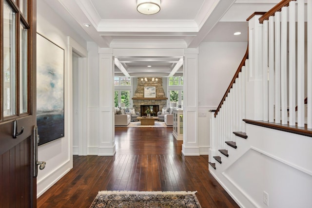 foyer entrance featuring dark wood finished floors, stairs, a stone fireplace, crown molding, and a decorative wall