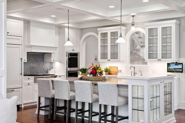 kitchen with coffered ceiling, white cabinets, tasteful backsplash, a kitchen bar, and beam ceiling